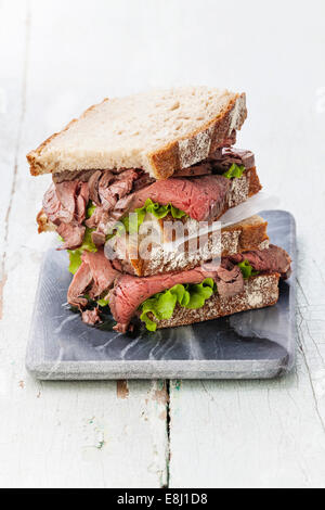 Roast Beef Sandwiches mit Salat auf Marmor Schneidebrett auf blauem Hintergrund Stockfoto