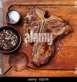 Gegrilltes t-Bone Steak mit Salz und Pfeffer auf Fleisch Schneidbrett auf dunklem Holz hautnah Stockfoto