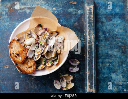 Vongole Muscheln mit Petersilie in Vintage Keramik Sieb auf blauem Hintergrund Stockfoto