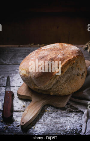 Frische hausgemachte Brot auf Holzbrett mit Vintage Messer diente über Holztisch mit Mehl Stockfoto