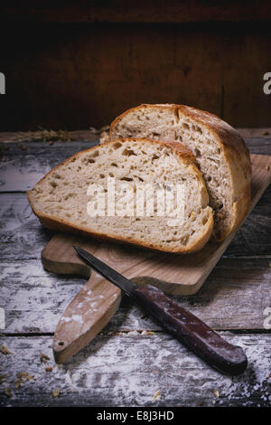 In Scheiben selbstgebackenes Brot auf Holzbrett serviert auf Holztisch mit Mehl Stockfoto