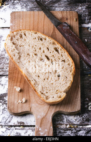 In Scheiben selbstgebackenes Brot auf Holzbrett mit Vintage Messer, serviert auf Holztisch mit Mehl. Ansicht von oben. Serien ansehen Stockfoto