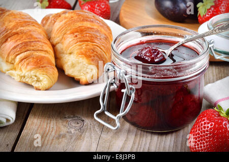 Erdbeer-Marmelade und Croissant auf Holztisch. Stockfoto