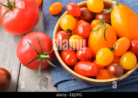 Bunte verschiedener Art Tomaten in einer Schüssel auf Holztisch. Rote, gelbe, große und kleine Tomaten. Stockfoto