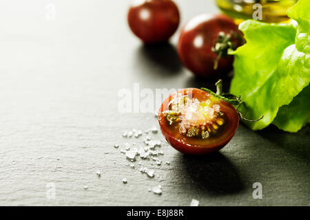 Frische Trauben Tomaten mit Salatblättern und Salz für den Einsatz als kochen Zutaten mit halbierten Tomaten im Vordergrund mit Exemplar Stockfoto