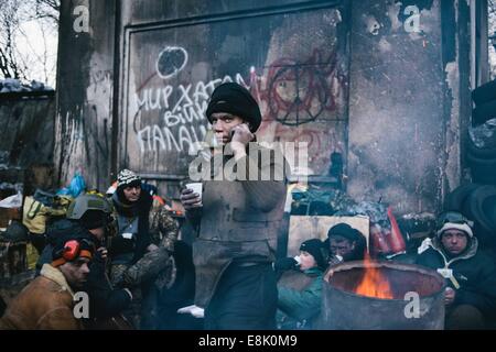 Kiew, Ukraine. 2. Februar 2014. Demonstranten sitzen durch ein Feuer als ein Mann spricht über ein Handy in der Nähe der Front an der Hrushevsk'koho Street. Masse Anti-Regierungs-Proteste im Zentrum von Kiew weiter. Die Front ist mit Schnee bedeckt, wie die angespannte Pattsituation auf Hrushevskoho Straße in der Nähe von Dynamo-Stadion, ein paar Blocks vom Epizentrum bei Majdan (Unabhängigkeitsplatz) weiter. (Kredit-Bild: © Jacob Balzani Loov/zReportage.com über ZUMA Press) Stockfoto