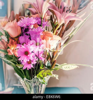 Nahaufnahme der Anordnung der lila, rosa & blass orange Blumen in einer Vase Klarglas. Stockfoto