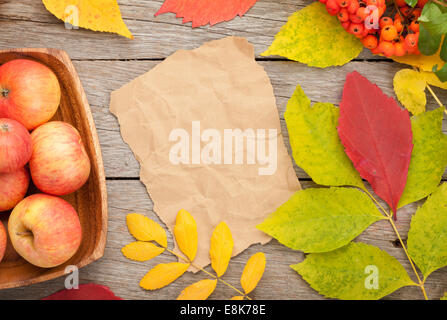 Herbstlaub, Vogelbeeren und Äpfel über Holz Hintergrund mit Papier für Textfreiraum Stockfoto