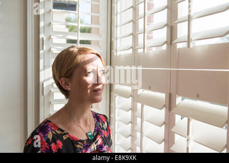 Eine Business-Frau / Mutter mit kurzen Haaren steht durch Jalousien in interessanten Licht Stockfoto