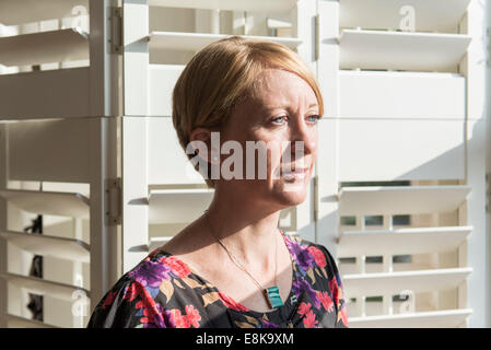 Eine Business-Frau / Mutter mit kurzen Haaren steht durch Jalousien in interessanten Licht Stockfoto