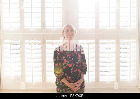 Eine Business-Frau / Mutter mit kurzen Haaren steht durch Jalousien in interessanten Licht Stockfoto