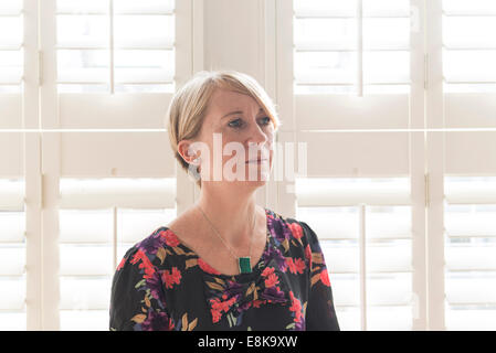 Eine Business-Frau / Mutter mit kurzen Haaren steht durch Jalousien in interessanten Licht Stockfoto