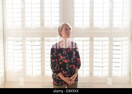 Eine Business-Frau / Mutter mit kurzen Haaren steht durch Jalousien in interessanten Licht Stockfoto