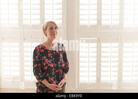 Eine Business-Frau / Mutter mit kurzen Haaren steht durch Jalousien in interessanten Licht Stockfoto