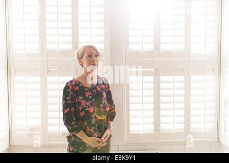 Eine Business-Frau / Mutter mit kurzen Haaren steht durch Jalousien in interessanten Licht Stockfoto