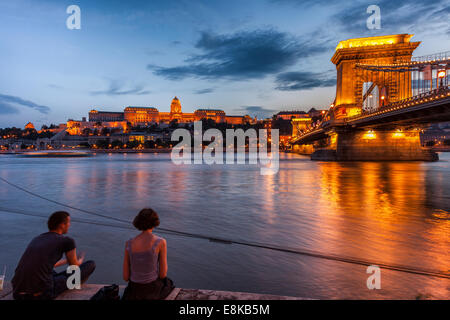 Junges Paar am Ufer auf Donau, Budaer Burg und Széchenyi Kettenbrücke in der Nacht, Budapest Ungarn Stockfoto