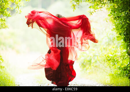 Scharlachrote Frau: Rückansicht eines Mädchens in einem blutroten Kleid Kleid im Wald Landschaft weglaufen Stockfoto