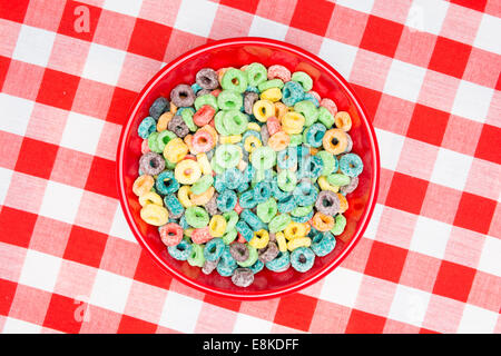 Eine rote Schale mit zuckerhaltigen geloopt süß Korn Getreide und Milch auf eine klassische, rot, karierte Tischdecke als Frühstück Mahlzeit bereit. Stockfoto