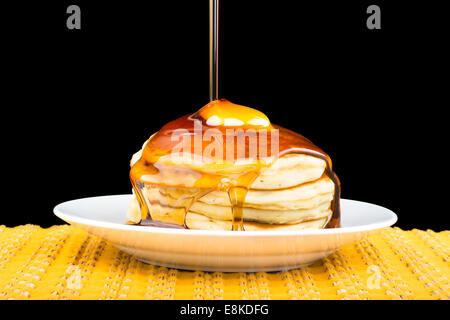 Süßer Ahornsirup über einen heißen, frisch gebutterte Stapel von Pfannkuchen gegossen wird. Stockfoto