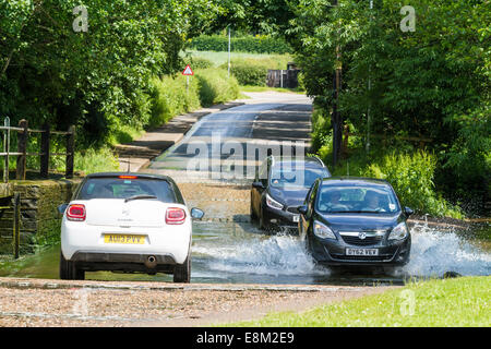 Autos fahren durch einen Stream. Auto wartet ein Ford zu überqueren, wie andere durch das Wasser auf der anderen Straßenseite in Rufford, Nottinghamshire, England, UK Antrieb Stockfoto