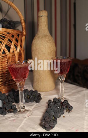 Korb Weide mit blauen schwere Ansammlung von süßen Trauben, Flasche und zwei Weinglas mit herben Rotwein Stockfoto
