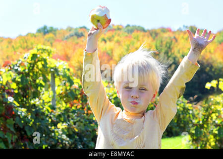 Ein glückliches Kind ist seine Arme in die Luft heben, wie er frisch geernteten Früchte auf einer Apfelplantage an einem sonnigen Herbsttag isst. Stockfoto