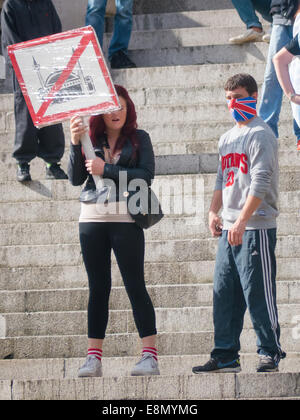 Eine Mädchen hält eine Anti Moschee Zeichen stehen neben einem Mann mit seinem Gesicht während ein English Defence League Protest in Portsmouth Guildhall Square, England von Anschluß-Markierungsfahne Maske bedeckt Stockfoto