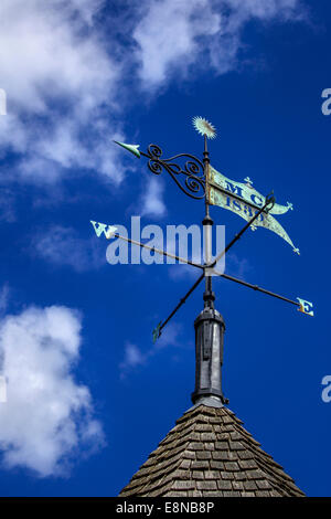 Wetterfahne auf einem sonnigen blauen Himmel mit weißen flauschigen Wolken. Wind Richtungspfeil zeigt west und hat eine leichte grüne Patina auf den Stockfoto