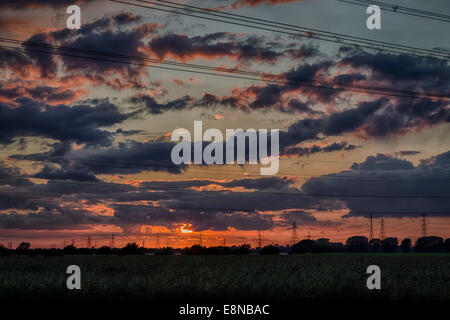 Sonnenuntergänge hinter Wolken mit Silhouetten von Strommasten in einem Feld. Stockfoto