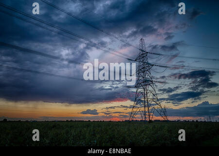 Strom Pylon Silhouette gegen einen blauen, violetten und orangefarbenen Himmel in der Abenddämmerung. Gewitterwolken am Horizont. Stockfoto