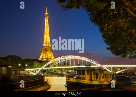 Dämmerung unter dem Eiffelturm, Flussschiffe und Fußgängerbrücke Passerelle Debilly entlang Seine, Paris, Frankreich Stockfoto