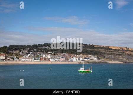 Ein kleines Fischerboot kehrt in Lyme Regis Hafen mit der Stadt von Lyme Regis und der Welt Erbe Jurassic Küste. Stockfoto