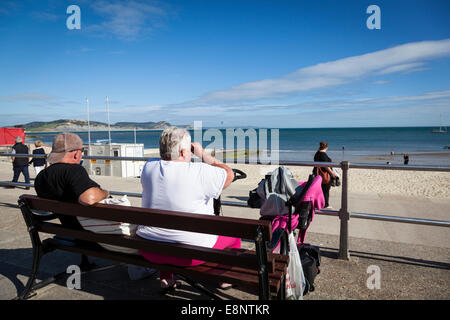 Paar, sitzen auf der Promenade bei Lyme Regis, Blick auf das Meer mit dem Fernglas. Stockfoto