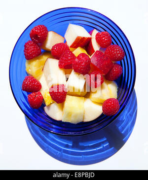 Draufsicht der Himbeeren, Apfel und Ananas in Kobaltblau Glasschale vor weißem Hintergrund Stockfoto