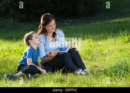 Junge Mutter lesen eine Geschichte Geschichte zu ihrem Sohn sitzt auf einem grünen Rasen im park Stockfoto