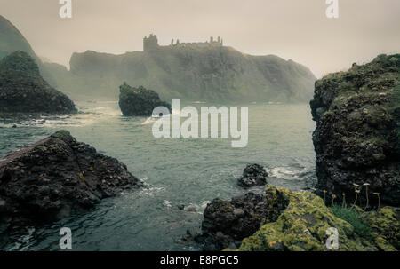 Neblige Ansicht von Dunnottar Castle, Aberdeenshire, Schottland. Aufgenommen vom Strand südlich des Schlosses. Felsen und Meer im Vordergrund sichtbar. Stockfoto