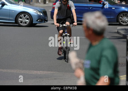 Ein Radfahrer nähert sich einen Mann über eine London-Straße - Verkehr im Hintergrund Stockfoto