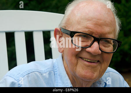 Porträt von ein älterer Herr in einem weißen Schaukelstuhl hautnah. Thema ist Lächeln auf den Lippen und auf der Suche von der Kamera entfernt. Stockfoto