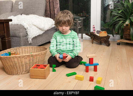 ein Junge spielt mit Holzklötzchen auf dem Boden im Wohnzimmer zu Hause Stockfoto