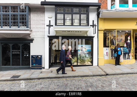 Mann und Frau Fuß vorbei an Geschäften auf der gepflasterten Guildford High Street während eine Frau ihr Handy überprüft. Stockfoto