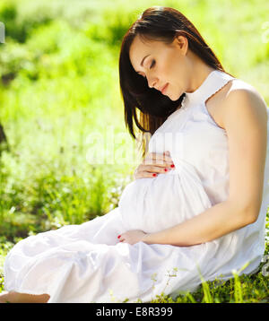 Porträt von schöne schwangere Frau in weißem Kleid im Frühlingspark Stockfoto