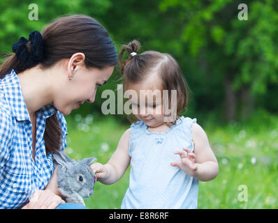 Niedliche kleine Mädchen und ihre Mutter umarmt wenig graue Kaninchen. Freundschaft und Pflege-Konzept Stockfoto