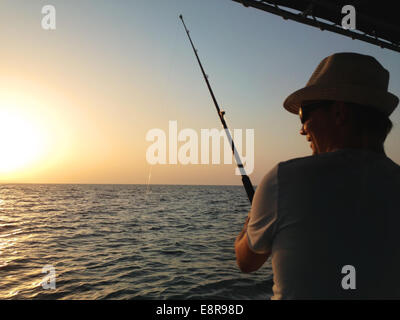 Junger Mann Angeln auf einem Ozean aus dem Boot bei Sonnenuntergang Stockfoto