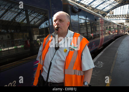 Ein Signal-Mann am Bahnhof bereitet seine Pfeife um den Fahrer wegzuziehen benachrichtigen zu blasen. Am Bahnhof von Brighton Stockfoto