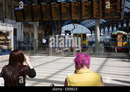 Passagiere warten auf Zug-Informationen auf dem Zusammentreffen am Bahnhof Brighton. Eine der Damen hat unverwechselbaren rosa Haare. Stockfoto