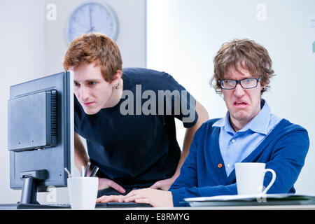 eine angewidert Büroangestellte während der andere sucht etwas in einem Computer-Bildschirm Stockfoto