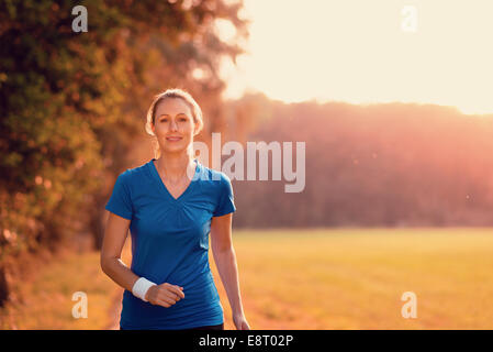 Attraktive aktive junge Frau, im strahlenden Morgenlicht auf einem Feldweg durch Wälder und Felder in einer Gesundheit ausüben, Stockfoto