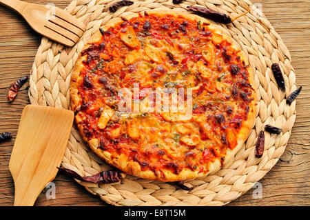 eine Pizza mit Hähnchen, Paprika und grünem Pfeffer, serviert auf einem hölzernen Hintergrund Stockfoto