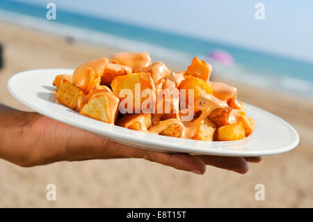 Nahaufnahme von einem Teller mit typisch spanische Patatas Bravas, Bratkartoffeln mit heißer Soße, am Strand Stockfoto