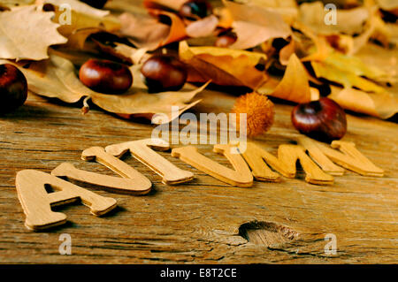 Holzbuchstaben bilden das Wort Herbst und einige Kastanien und Herbst Blätter auf einem verwitterten hölzernen Hintergrund Stockfoto